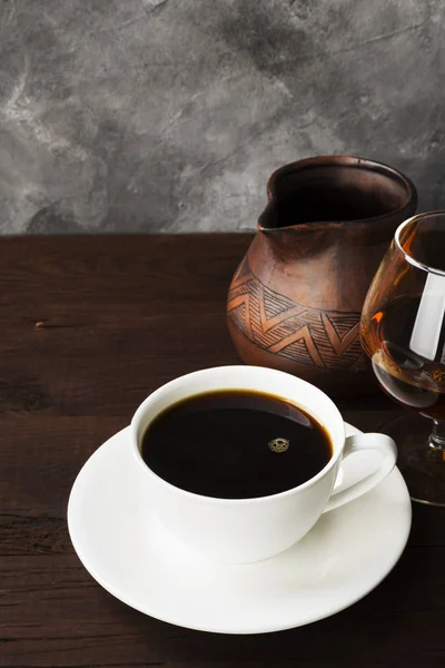 Coffee in white cup with cognac and clay cezve on wooden backgro — Stock Photo, Image