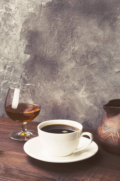 Café em copo branco com conhaque e cezve de barro em backgro de madeira — Fotografia de Stock