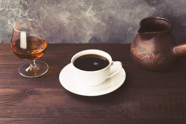 Coffee in white cup with cognac and clay cezve on wooden backgro — Stock Photo, Image