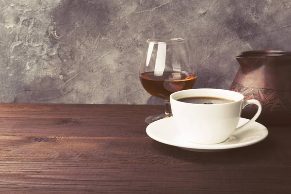 Coffee in white cup with cognac and clay cezve on wooden backgro — Stock Photo, Image