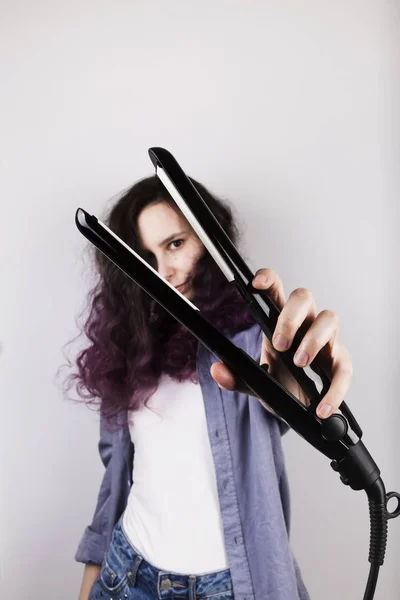 Молодая девушка выпрямляет вьющиеся волосы из плоского железа. Фиолетовый цвет — стоковое фото