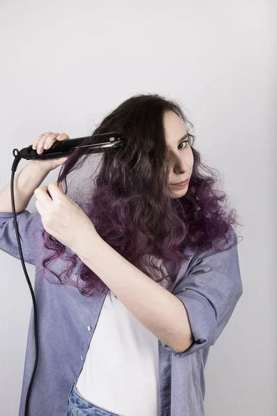 Young girl straightens curly hair of Flat Iron. Coloring purple