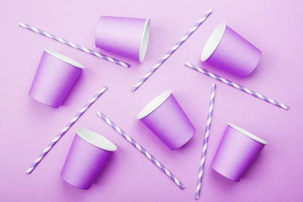 Purple paper cups and purple-white straw on purple background