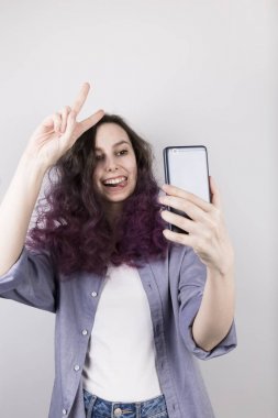 Genç kız selfie çekiyor. Kıvırcık boyama mor saç. Gri backgr