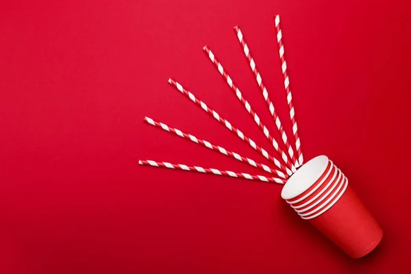 Red paper cups and red-white straw on red background. Top view,