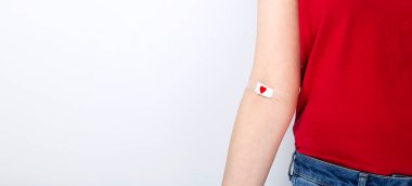 Kan bağışı. Kırmızı tişörtlü genç kız. Gri arka planda kan verdikten sonra kırmızı kalple bantlanmış. Boşluğu kopyala