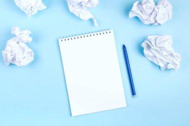Kırışmış kağıtların etrafında mavi arka planda beyaz defter ve kalem. Plan hazırlama, kötü fikirlerden kurtulma kavramı. Düz yatıyordu. Boşluğu kopyala