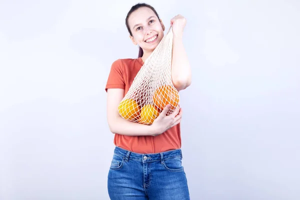 Menina Jovem Pressiona Saco Cordas Com Laranjas Sorrisos Fundo Cinza — Fotografia de Stock