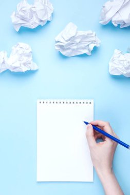Kadın not defterine buruşmuş kağıtların etrafına mavi arka planda bulut şeklinde yazıyor. Dilek listesi ve hayaller çizme kavramı, bulutlara yönel