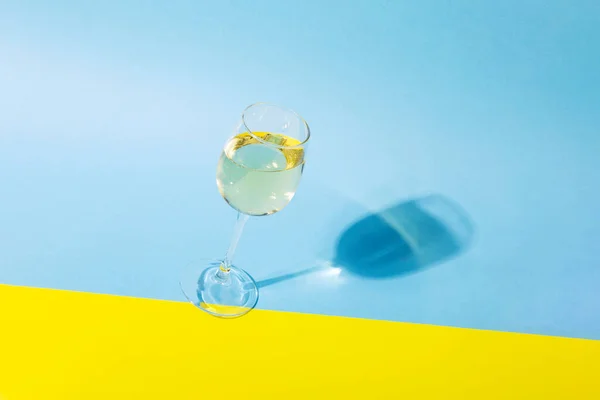 白ワインのガラスは ガラスから黄色の青の背景 長い影に傾いている 影絵効果ハードライト ストック写真