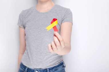 Dünya Hepatit Günü kavramı. Gri tişörtlü kız elinde kırmızı-sarı kurdele sembolü tutuyor. Gri arka plan. Boşluğu kopyala