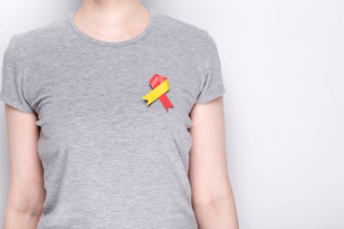 Dünya Hepatit Günü Konsepti. Üzerinde kırmızı-sarı kurdele olan gri tişörtlü bir kız. Gri arka plan. Boşluğu kopyala