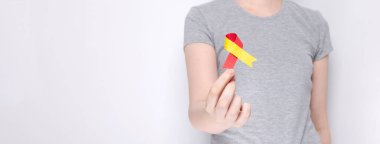 Dünya Hepatit Günü kavramı. Gri tişörtlü kız elinde kırmızı-sarı kurdele sembolü tutuyor. Gri arka plan. Boşluğu kopyala
