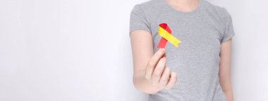 World Hepatitis Day concept. Girl in gray T-shirt holds in her hand awareness symbol red-yellow ribbon. Gray background. Copy space clipart