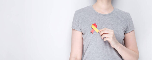 World Hepatitis Day concept. Girl in gray T-shirt holds in her hand awareness symbol red-yellow ribbon. Gray background. Copy space