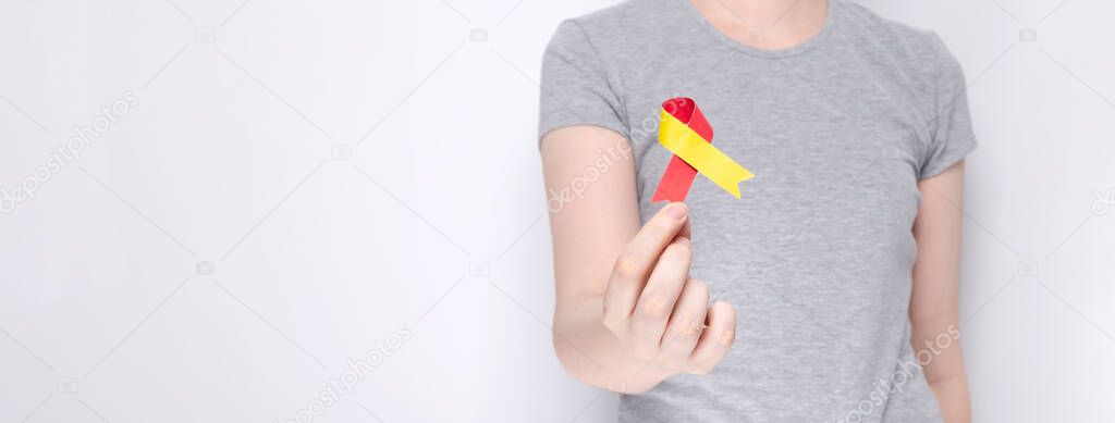 World Hepatitis Day concept. Girl in gray T-shirt holds in her hand awareness symbol red-yellow ribbon. Gray background. Copy space