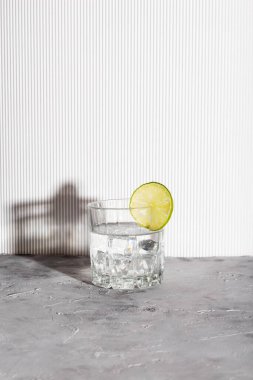 Buzlu votka ve gri arka planda gözlüklü limon. Gölgeler ve güneş ışığı modası