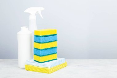 Çeşitli deterjan ürünleri ajanı, bir yığın sünger ve temizlik peçetesi, gri arka plan. Boşluğu kopyala