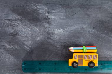 Okul konseptine geri dönelim. Okul otobüsündeki okul gezisinin taklidi. Kalemler, cetvel, kalemtıraş, siyah arka planda oyuncak otobüs. Üst Manzara. Boşluğu kopyala