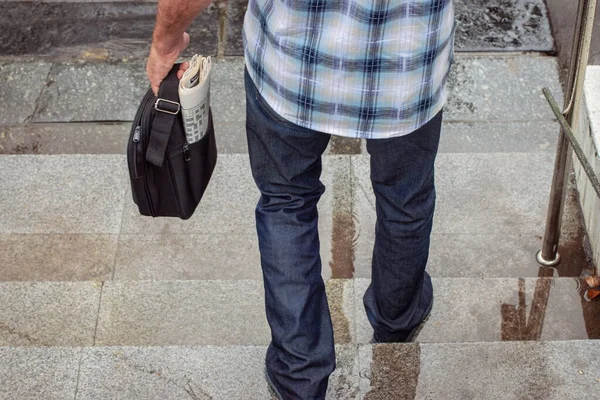 Legs and hand of an elderly man with a bag and a newspaper that contains a crossword puzzle