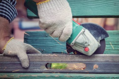 Bir testere öğütücüsü, sürtünme kıvılcımları uçuşurken, eldivenle metal bir bilye keser ve onu elleriyle tutar.