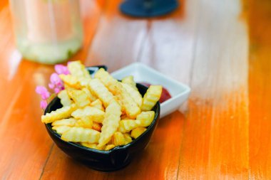 Lokantada aperatif olarak servis edilen beyaz bir kasede patates kızartması ve ahşap bir masada ketçap.