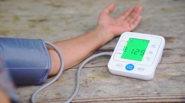 Tahta bir masanın üzerinde otomatik dijital monitörle kan basıncını ölçen kişinin yakın çekimi, sistolik, diyastolik ve nabız ölçümleri sağlık kontrolü ve tıbbi bakım konseptleri için.