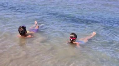 İki çocuk deniz kenarında keyifli bir sahneyle meşgul olur, biri zarifçe yüzerken diğeri şakacı bir şekilde oturur, yaz maceralarının kaygısızca özünü gözler önüne serer ve su keyfi yapar.