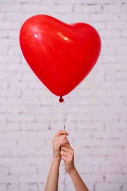 Kırmızı kalp balon tutan kadın eller ve tuğla duvar stüdyosu arka planda poz, Doğum günü partisi kavramı 