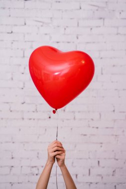 Kırmızı kalp balon tutan kadın eller ve tuğla duvar stüdyosu arka planda poz, Doğum günü partisi kavramı 