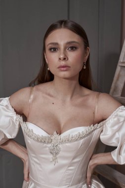 Stüdyodaki ahşap merdivenin yanında poz veren şık, uzun gece elbisesi içinde güzel esmer kadın.   