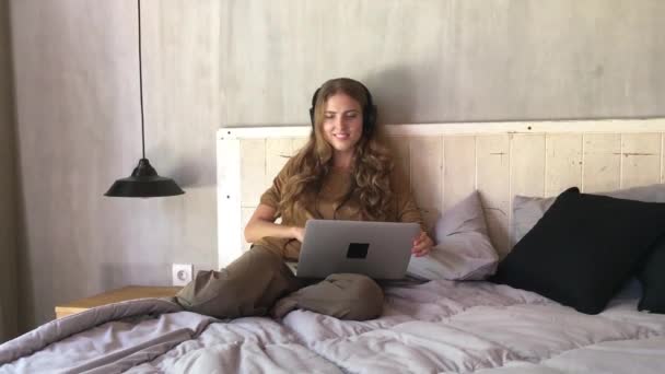 美丽的女人在耳机听音乐从笔记本电脑 而坐在卧室的床上 — 图库视频影像