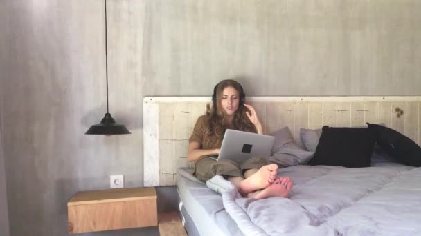 美丽的女人在耳机听音乐从笔记本电脑 而坐在卧室的床上 — 图库视频影像