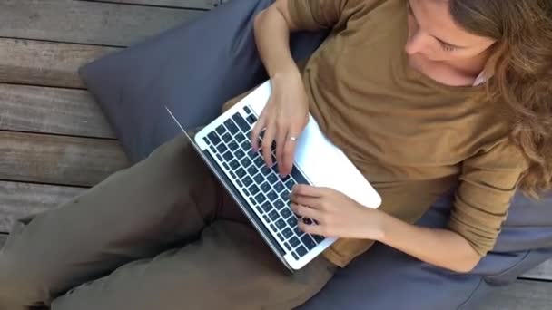 Jovem Mulher Mensagens Texto Laptop Enquanto Sentado Cadeira Beanbag Terraço — Vídeo de Stock