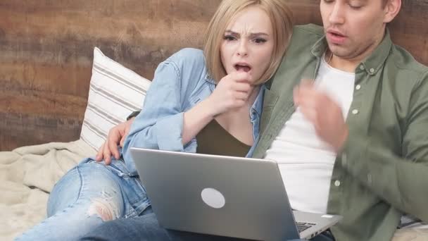 Young European couple watches a scary movie on laptop lying on bed in their bedroom — Stock Video