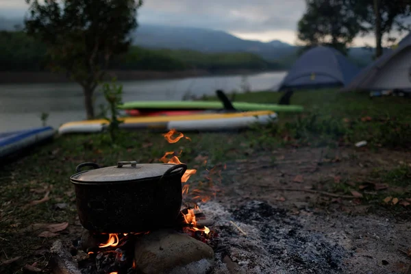 Camp and cooking in field conditions, boiling pot at the campfire on picnic in morning. Cooking dinner on firewood stove using firewood when going to the wilderness or outdoor activity, camping tent