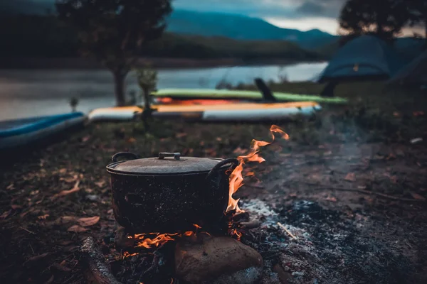Camp and cooking in field conditions, boiling pot at the campfire on picnic in morning. Cooking dinner on firewood stove using firewood when going to the wilderness or outdoor activity, camping tent