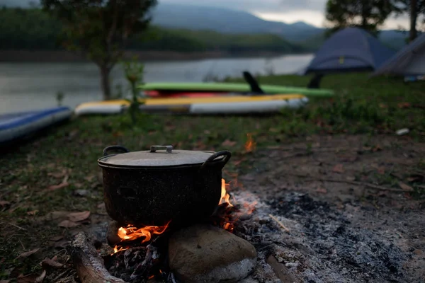 Camp and cooking in field conditions, boiling pot at the campfire on picnic in morning. Cooking dinner on firewood stove using firewood when going to the wilderness or outdoor activity, camping tent