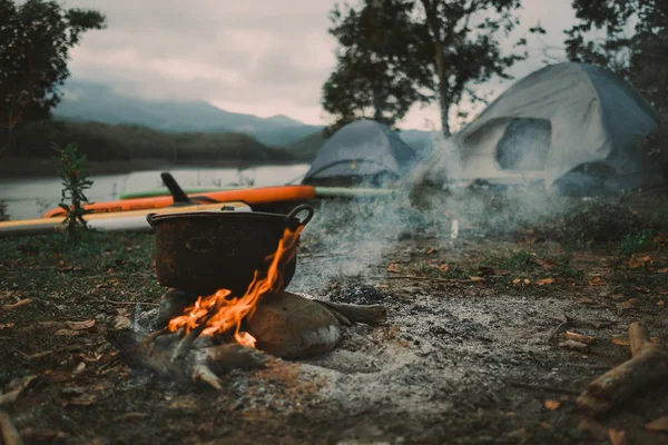 Camp and cooking in field conditions, boiling pot at the campfire on picnic in morning. Cooking dinner on firewood stove using firewood when going to the wilderness or outdoor activity, camping tent