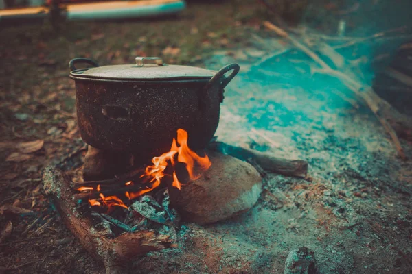 Camp and cooking in field conditions, boiling pot at the campfire on picnic in morning. Cooking dinner on firewood stove using firewood when going to the wilderness or outdoor activity, camping tent