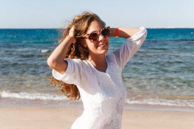 yakın çekim dalgaları ile mavi deniz ve gökyüzü bulutlu bir güneşli gün, yaşam tarzı, poz ve gülümseyen, Rüzgar bir arka plan üzerinde uzun saçlı güzel bir genç esmer kız portresi.