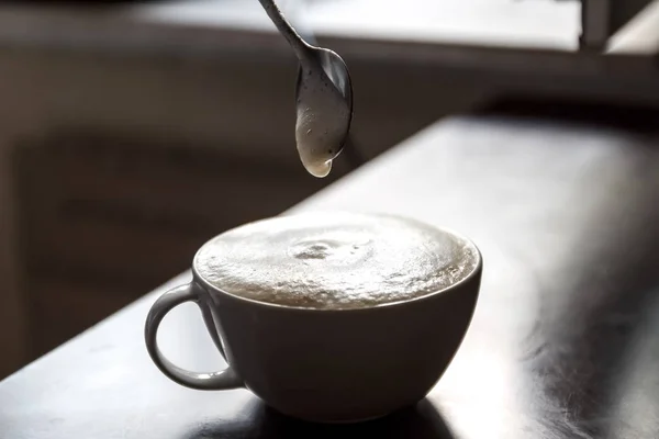 Cup of coffee with foam being stirred by a human hand.