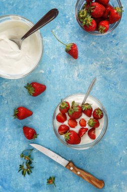 Organik yoğurt bir kase taze çilek mavi bir beton zemin üzerinde kesti. Üstten görünüm ve yakın çekim. Flatlay.