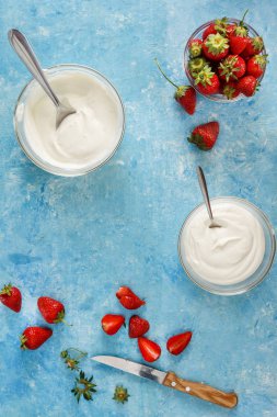 Organik yoğurt bir kase taze çilek mavi bir beton zemin üzerinde kesti. Üstten görünüm ve yakın çekim. Flatlay.
