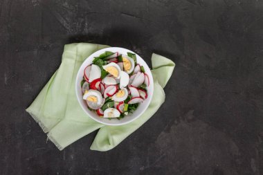 Sebze vejetaryen salata ramson, turp, yeşil soğan ve çatal bıçak takımı peçeteye retro işlemedeki karanlık bir beton zemin üzerine beyaz bir tabak yoğurt sos ile haşlanmış yumurta. Yakın çekim, en iyi görünüm, flatlay. Sağlıklı beslenme kavramı