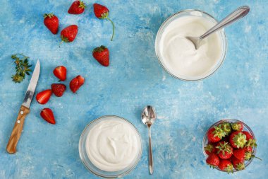 Organik yoğurt bir kase taze çilek mavi bir beton zemin üzerinde kesti. Üstten görünüm ve yakın çekim. Flatlay.
