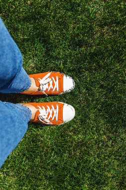 Yeşil çimenlerin üzerinde eski sarı spor ayakkabılar bacaklar. Yukarıdan görüntüleyin. Gençlik, Bahar ve özgürlük kavramı.