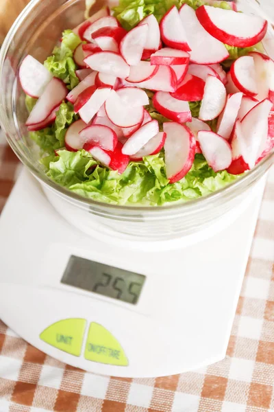 Dietary salad with radish and lettuce in a glass bowl standing on the kitchen scales. The concept of proper healthy healthy dietary nutrition. Counting calories and weight loss products