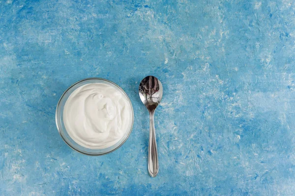 Greek yogurt in a bowl with a spoon, close-up on blue stone table top view