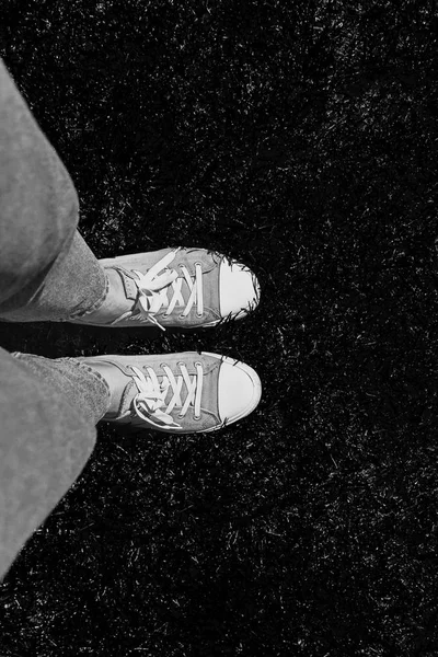 Legs in old sneakers on grass. View from above. Style: abstraction, illustration, monochrome, neon.